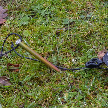 Titanium rainbow tent peg secured in grass beside a hiking boot